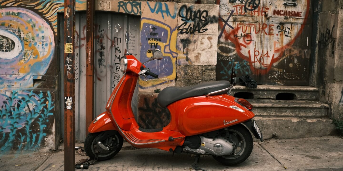 Scooter rouge garé de profil le long d'un mur couvert de graffitis